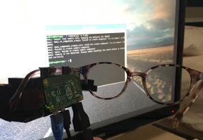 Photo of the prototype (glasses with an Arduino attached) in front of a computer screen with code displayed.