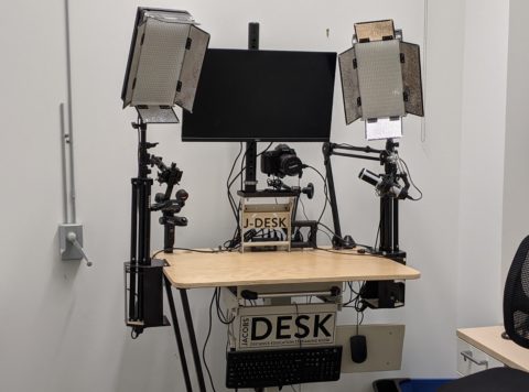 A kiosk with electronics equipment, including a monitor, two studio lights, and a DSLR camera